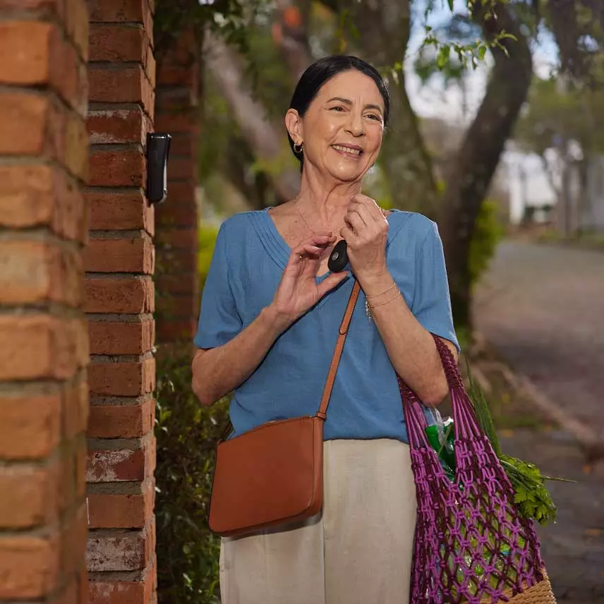 Dona Tereza sorrindo na calçada, junto do seu aparelho da TeleHelp.